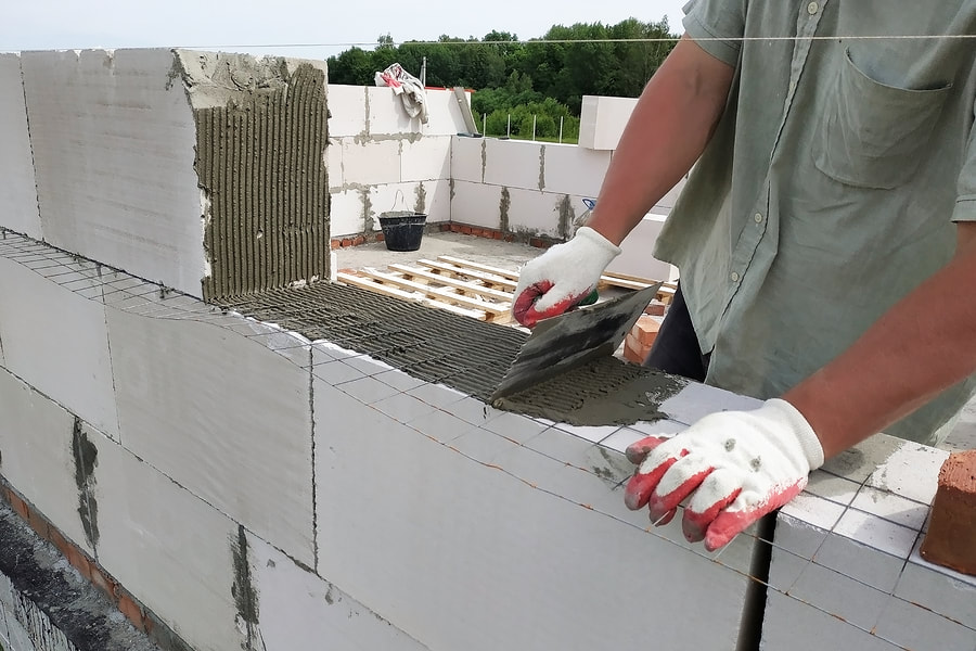 man putting a cement on the top of the bricks to make it wall